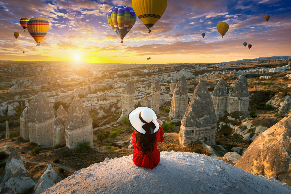 Woman,Sitting,And,Looking,To,Hot,Air,Balloons,At,Sunrise